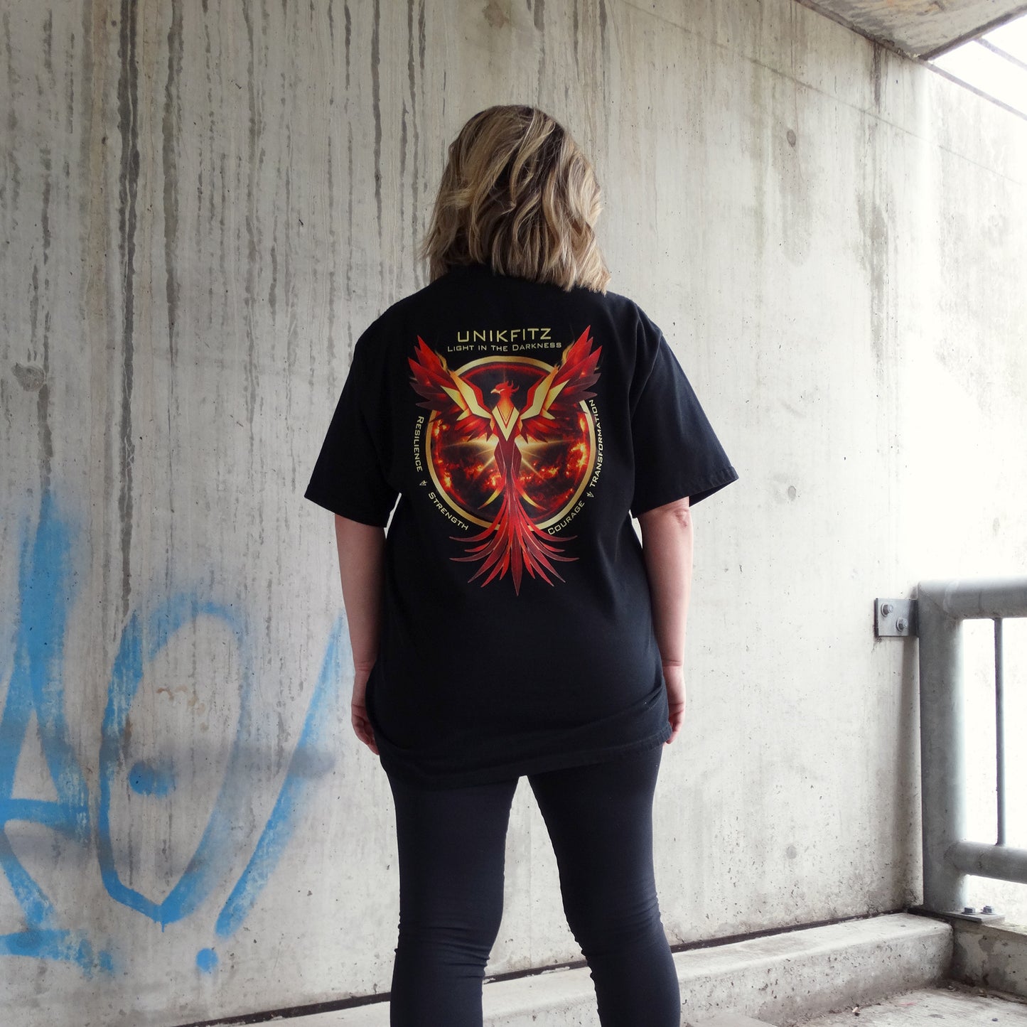 The Rise & Soar Women's T-Shirt in black, featuring a striking phoenix graphic with the words 'UNIKFITZ - Light in the Darkness.' A bold piece of Australian streetwear for women, designed for gym wear and everyday style. This essential women's t-shirt blends resilience with street wear aesthetics