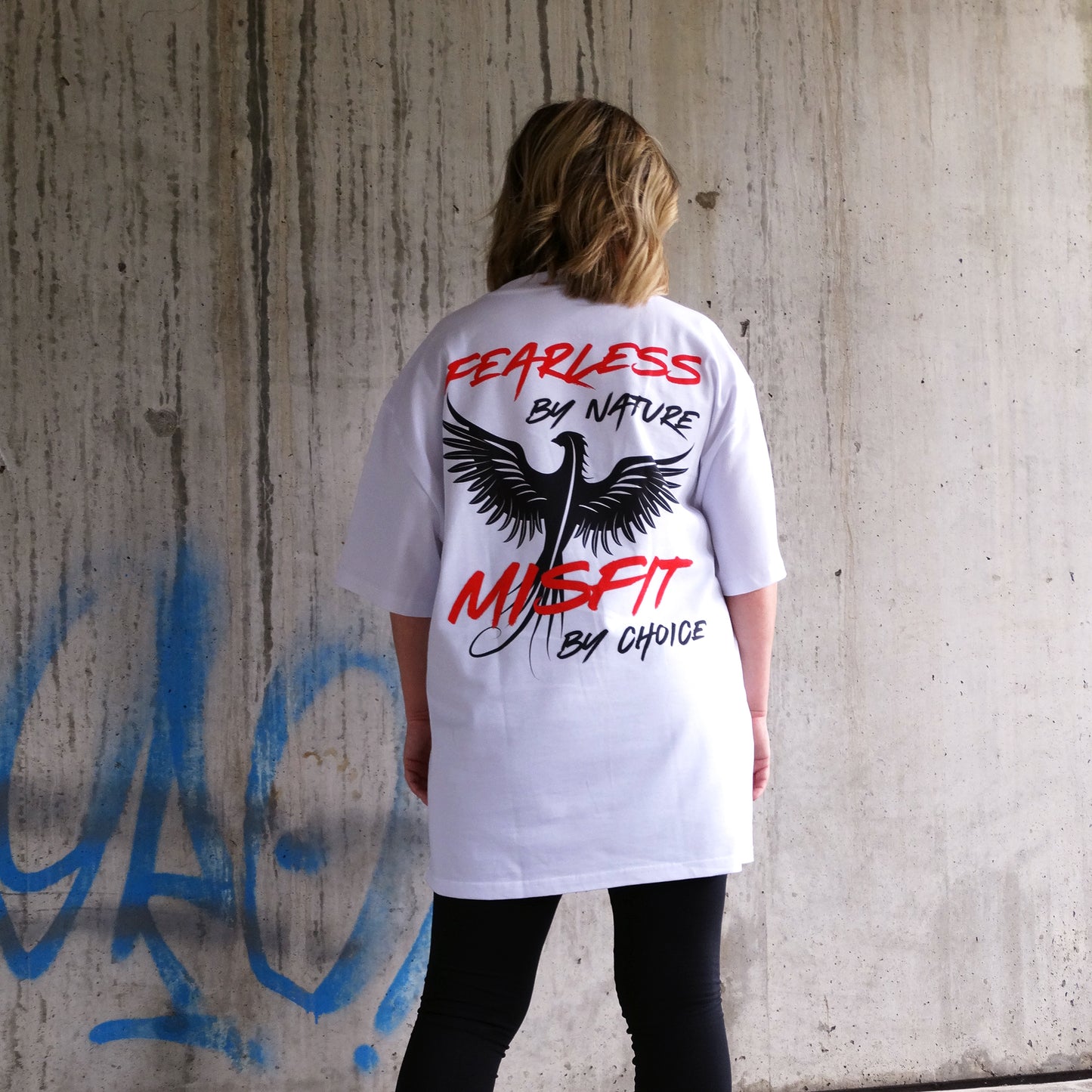 A dynamic shot of a model walking up the stairs in the Rise & Soar Women's T-Shirt in white, displaying its oversized fit and phoenix graphic print on the back. This statement women's wear piece combines Australian streetwear culture with essential t-shirt styling for an edgy, fearless look.