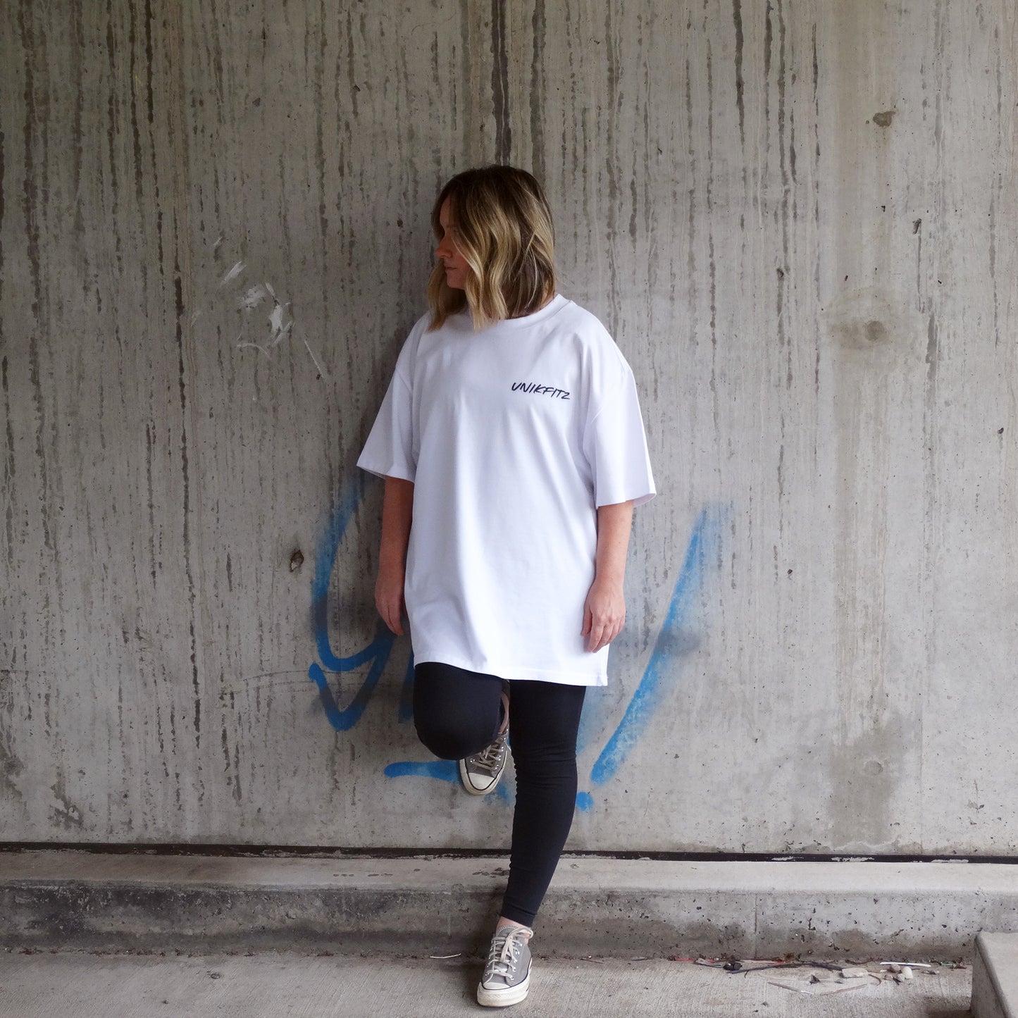 Close-up front view of a model wearing the Rise & Soar Women's T-Shirt in white by UNIKFITZ, featuring a minimalist streetwear aesthetic with a bold logo. This oversized fit essential t-shirt for women is a premium piece of Australian streetwear, perfect for casual and gym wear.