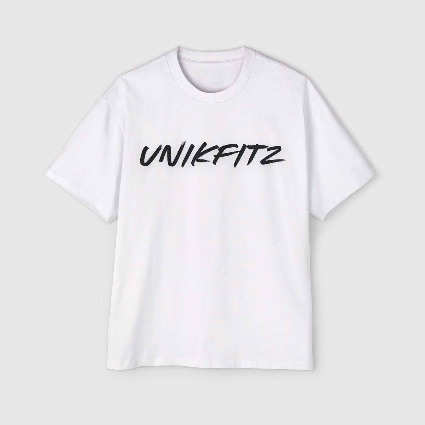 A crisp white oversized T-shirt laid flat, featuring the bold black 'UNIKFITZ' logo in graffiti-style font across the chest. This piece of active street wear for the fearless misfits delivers a clean and empowering look for modern trendsetters