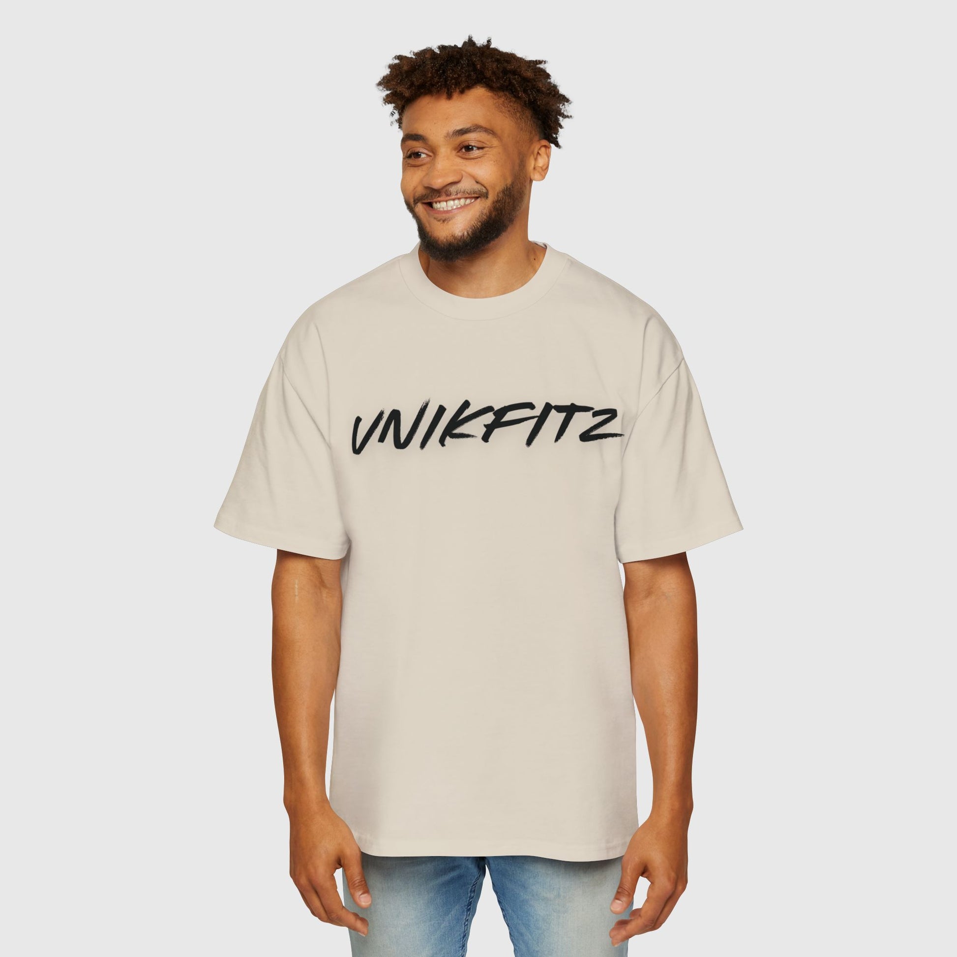 A smiling man wearing a beige oversized T-shirt with 'UNIKFITZ' printed in bold black brushstroke font across the chest. This active street wear that motivates showcases a clean and stylish design perfect for everyday wear