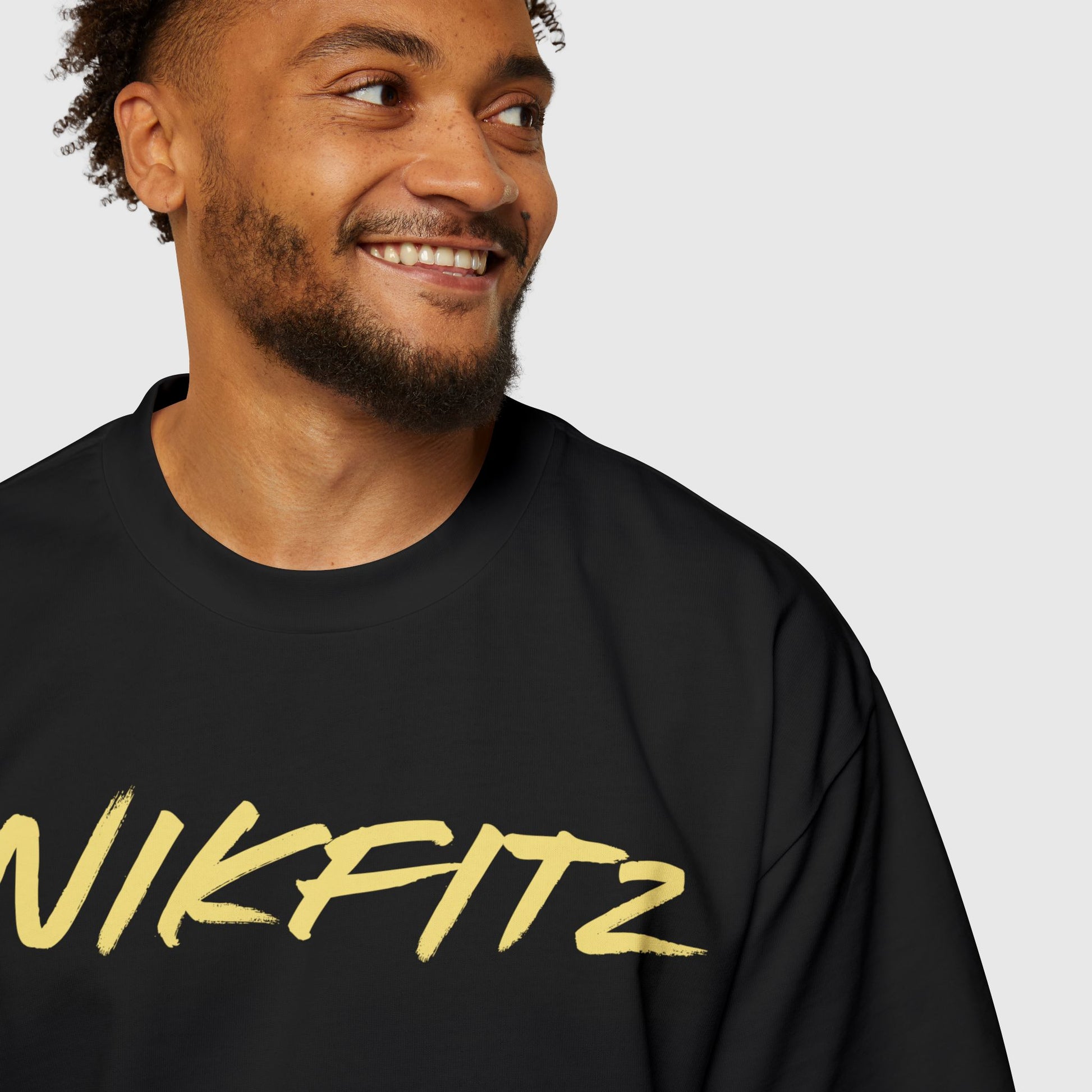 Close-up of a smiling man wearing a black UNIKFITZ T-shirt with prominent yellow branding, ideal for gym-ready street wear or casual men's clothing enthusiasts seeking essential sweatshirts with a stylish edge.