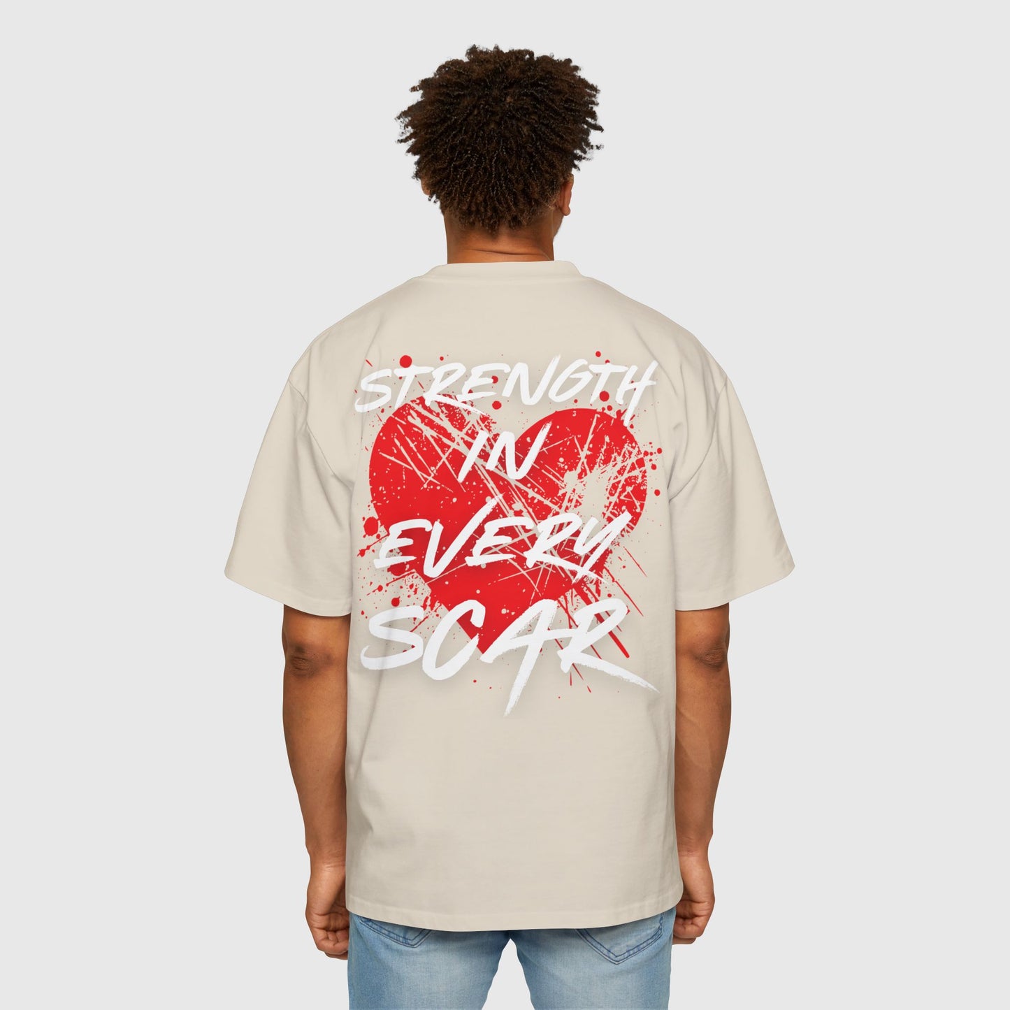 Back view of a man in a beige oversized men’s t-shirt with bold red heart graffiti art and "Strength in Every Scar" text – men’s clothing gym, street wear, men’s t-shirt essential.