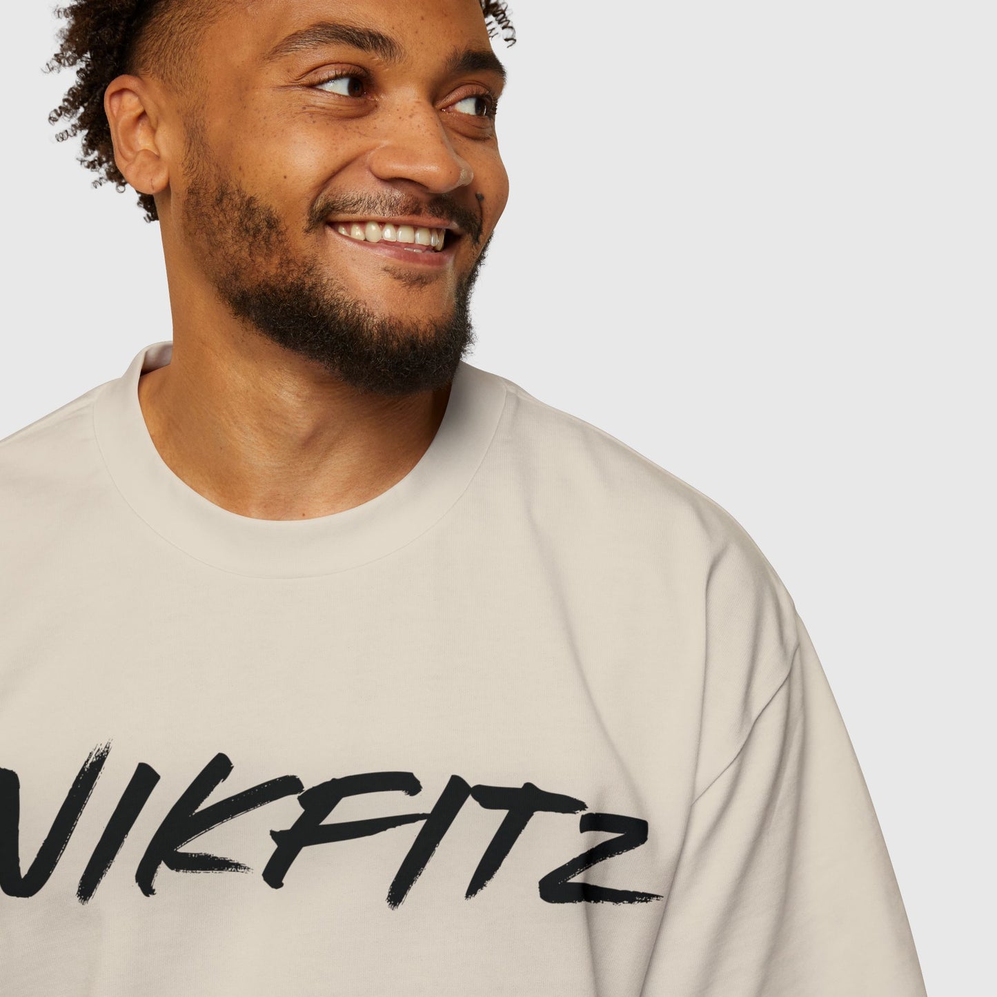 Close-up of a man wearing an off-white oversized T-shirt with 'UNIKFITZ' written in bold black brushstroke font, showcasing minimalistic men's streetwear fashion.