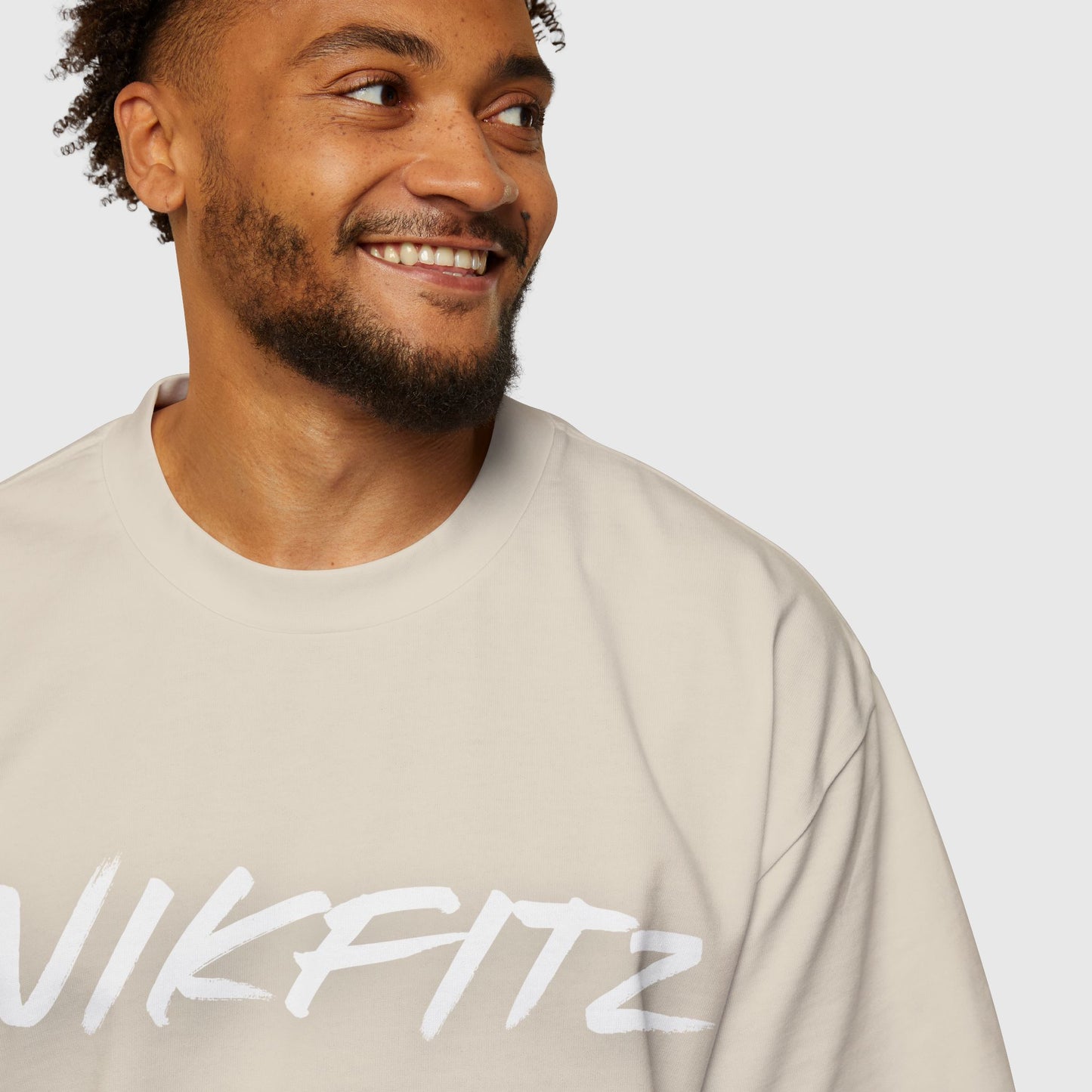 A close-up of a man wearing a beige oversized sweatshirt with the "UNIKFITZ" logo in white. A minimalist design for men's clothing, offering comfort and style for casual or gym wear