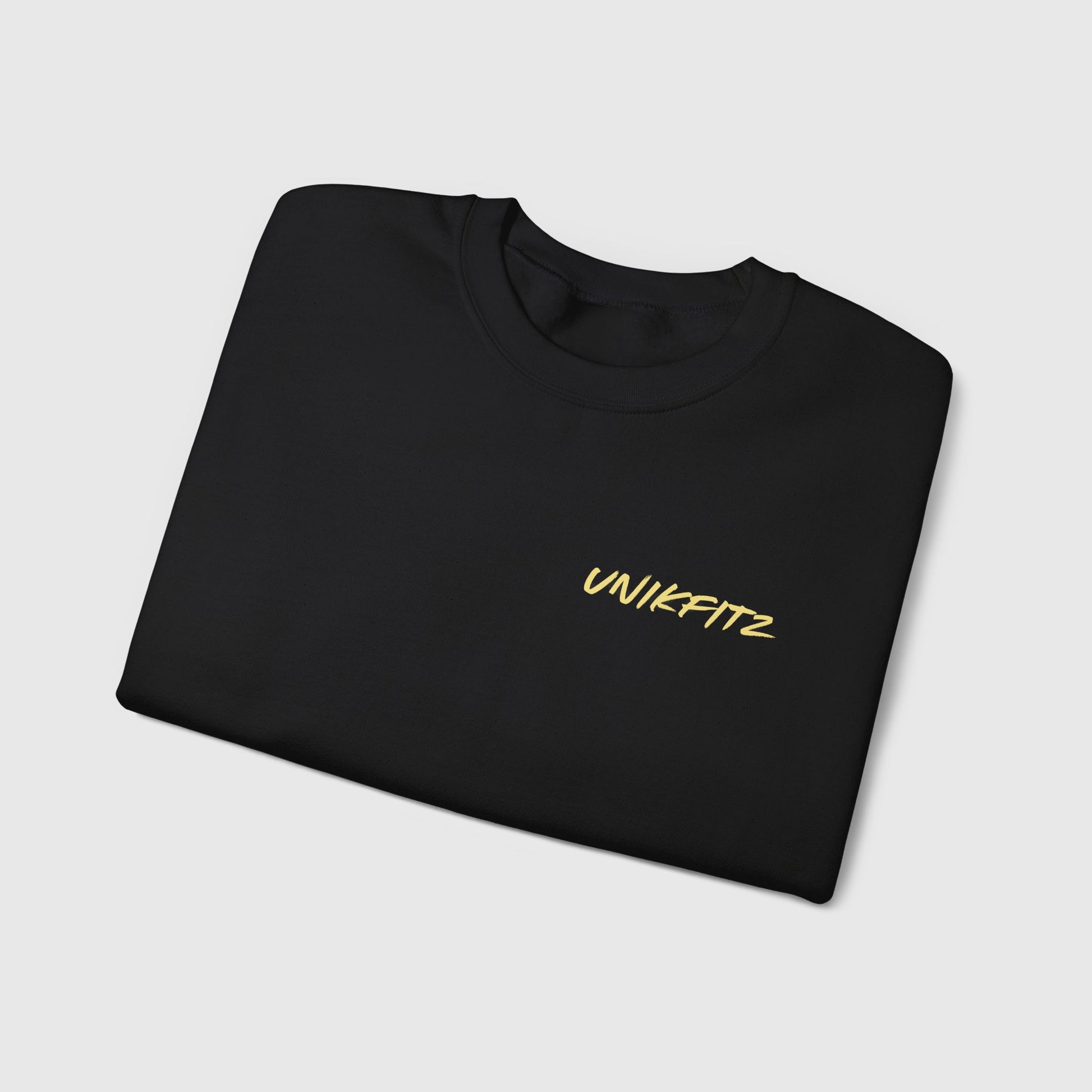 Black essential sweatshirt with a minimalist 'UNIKFITZ' logo in bold yellow text, perfectly folded. A premium piece in men's clothing, ideal for gym and streetwear enthusiasts.