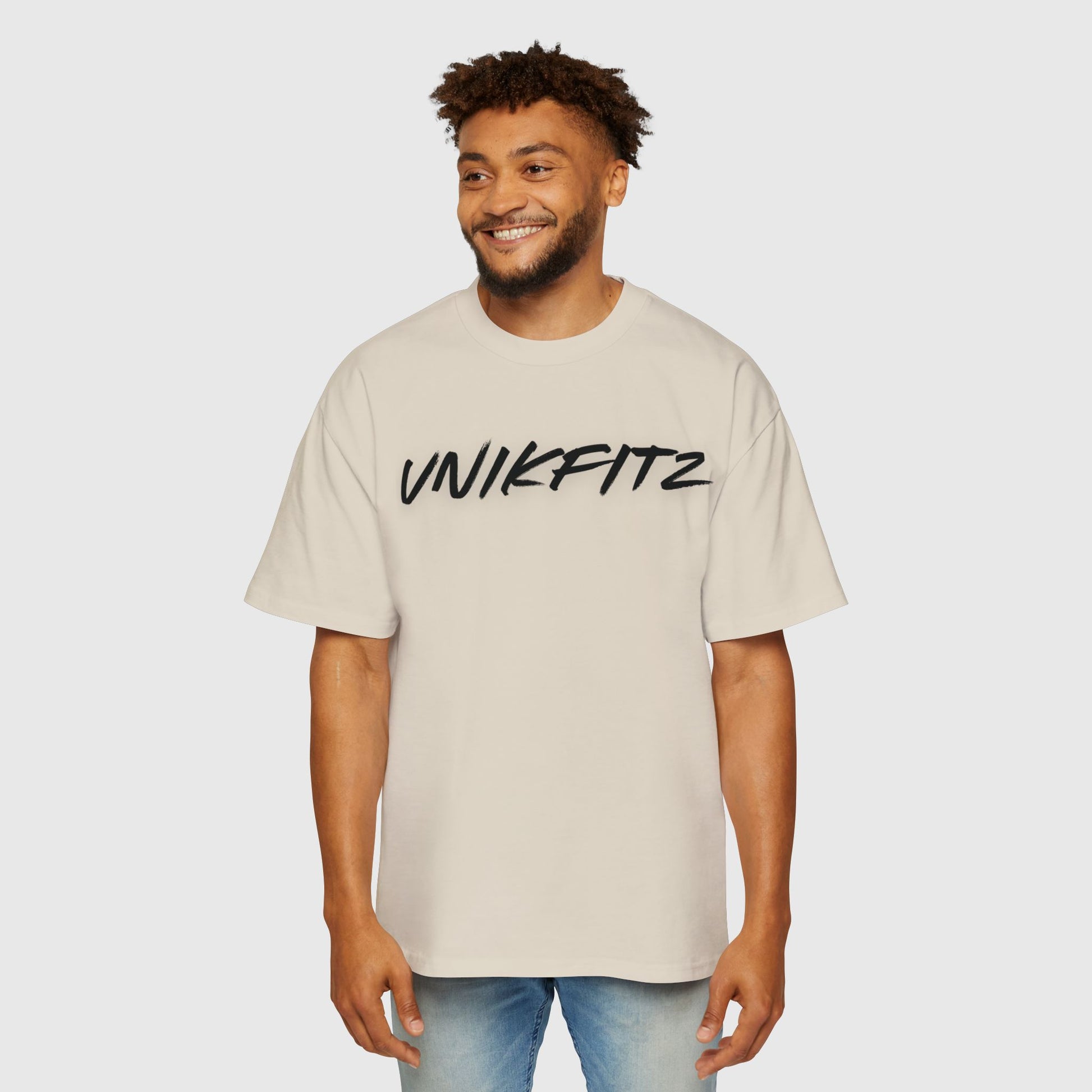 Man confidently posing in a cream oversized T-shirt featuring 'UNIKFITZ' logo, a trendy essential for men's wear