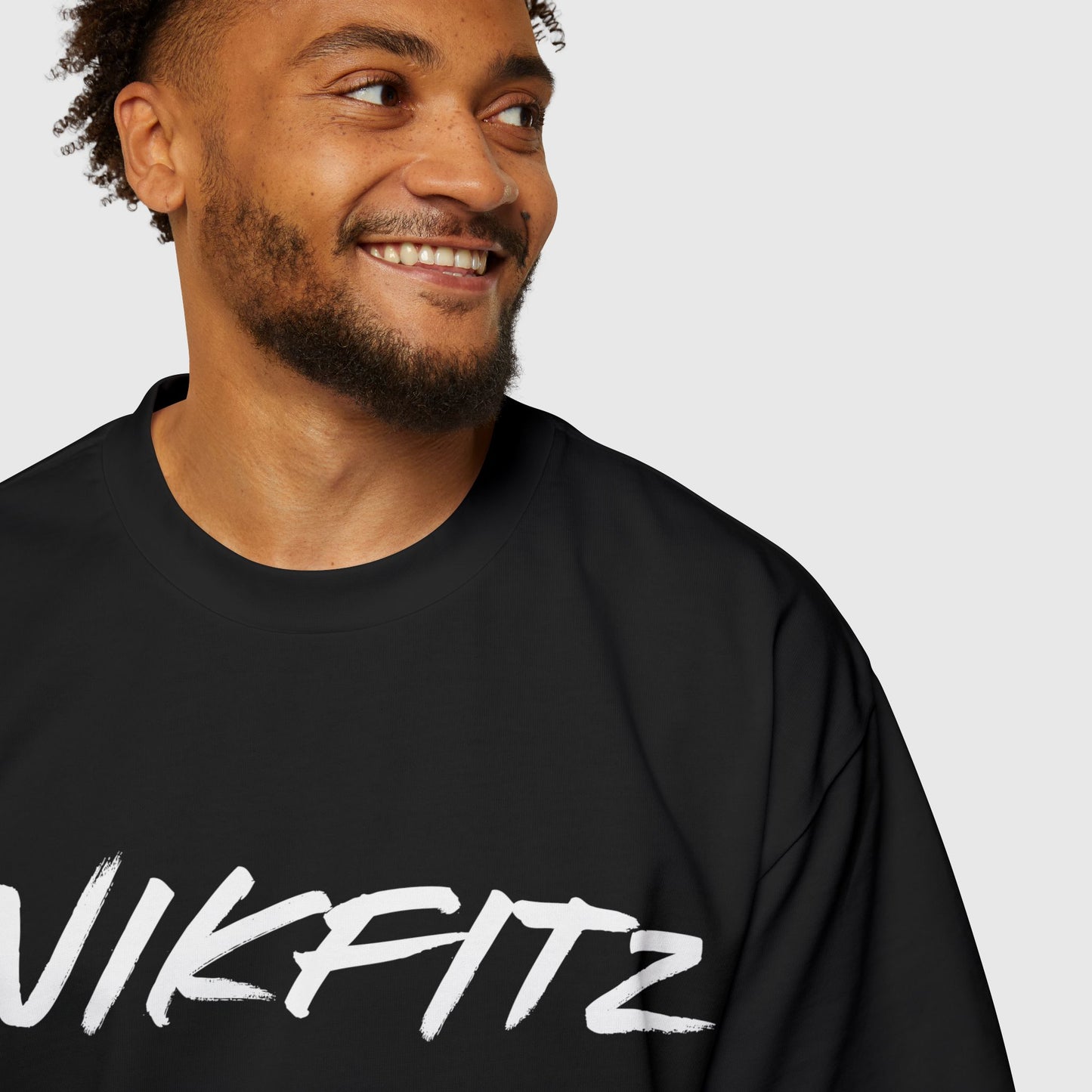 Close-up view of a man smiling in a black oversized t-shirt featuring the bold "UNIKFITZ" logo in white, ideal for casual men's clothing, street wear, or essential sweatshirts.