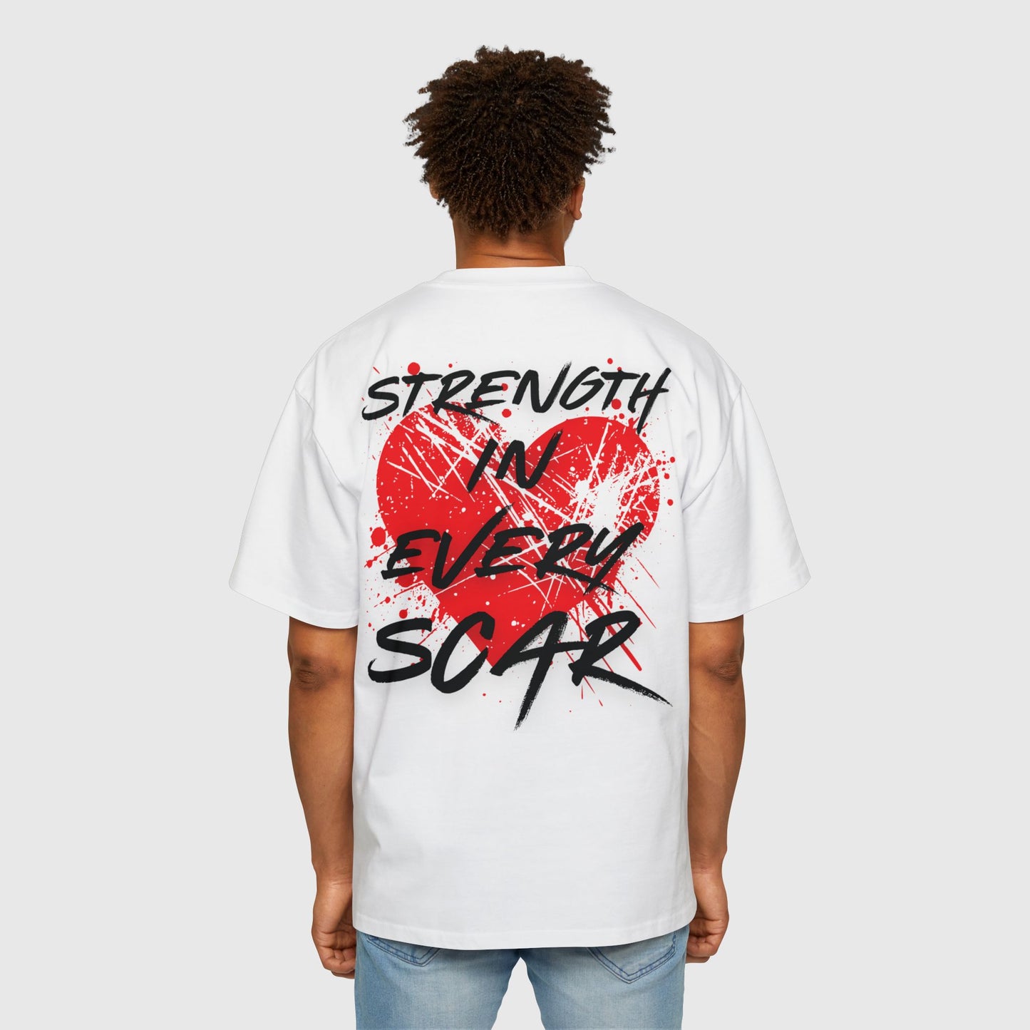 A man wearing a white oversized T-shirt with a bold red splattered heart and the motivational slogan 'Strength in Every Scar' printed on the back. This active street wear that motivates combines comfort with an artistic, empowering message.