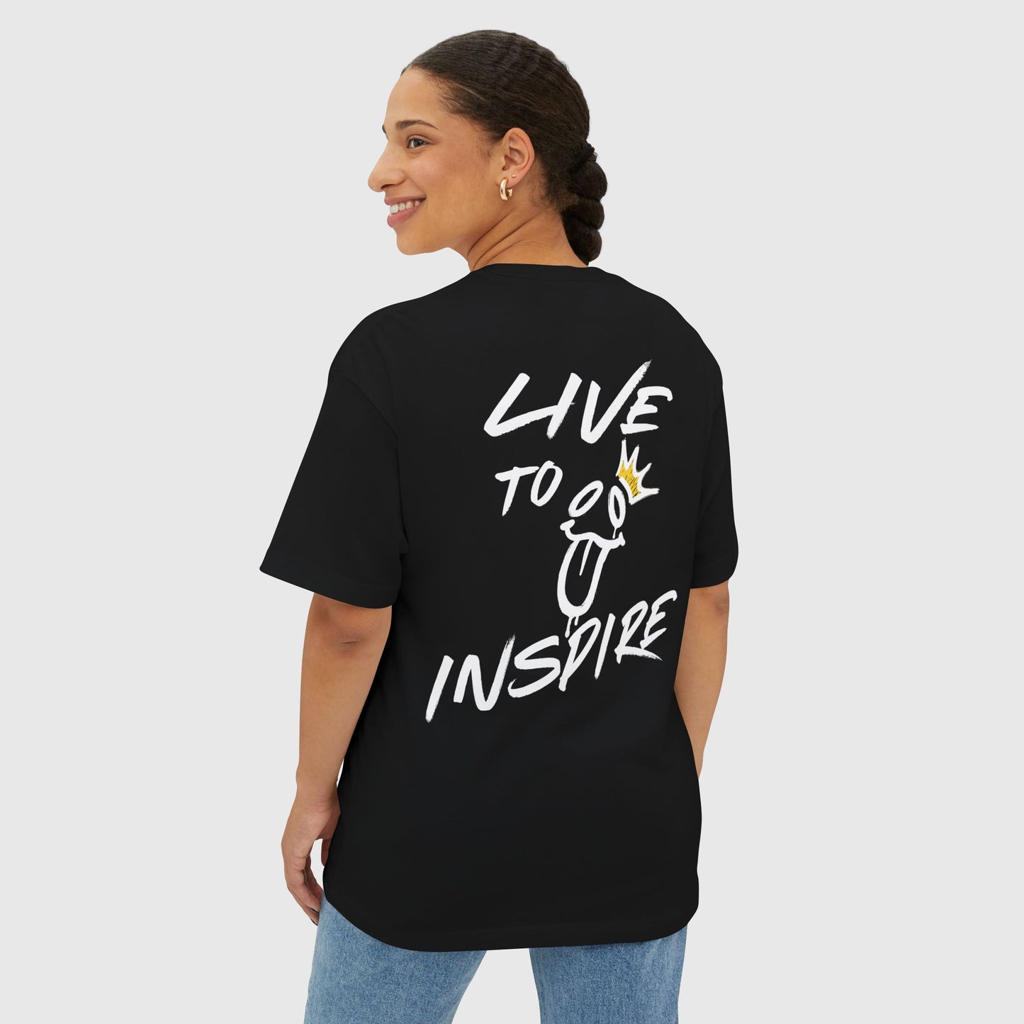 The back view of a black oversized T-shirt featuring the bold "Live to Inspire" graphic with playful illustrations in white and gold. A statement piece in women's clothing for gym or streetwear enthusiasts