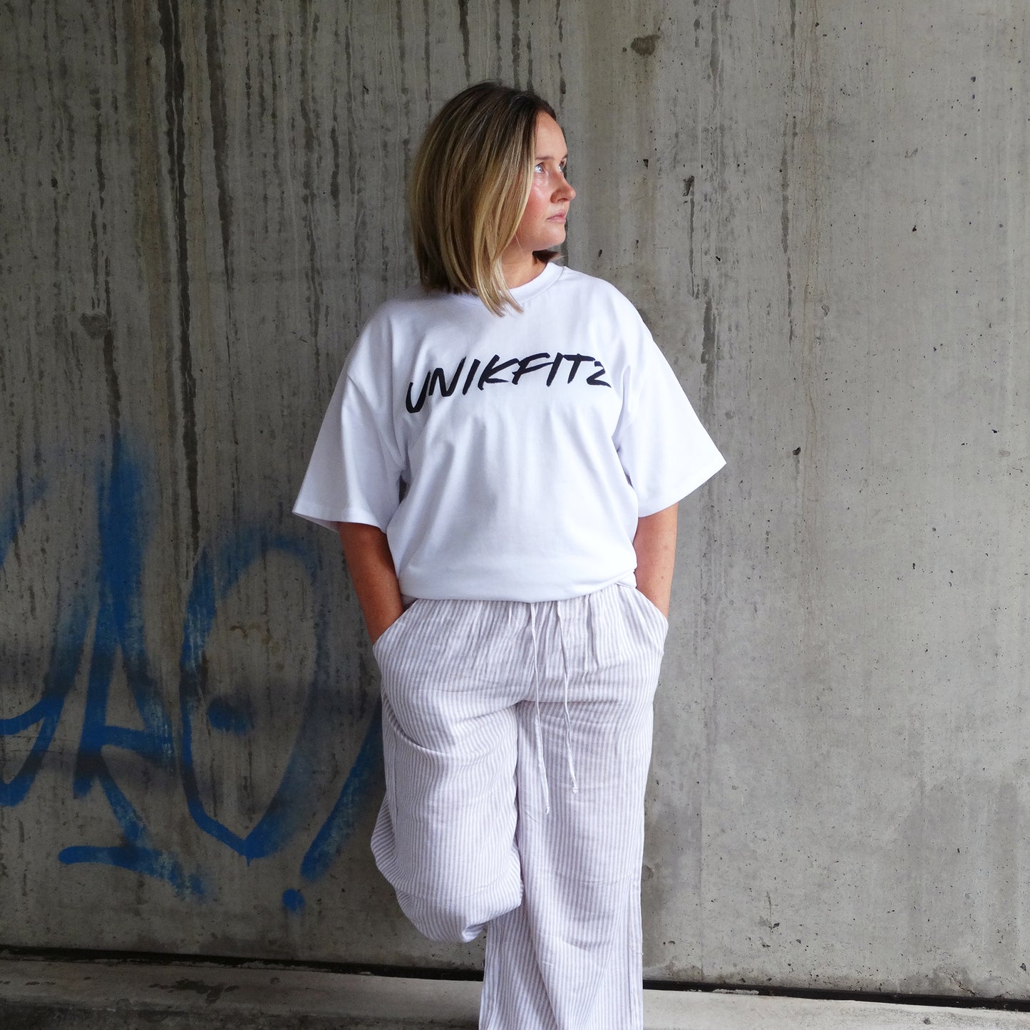 Model wearing the white 'Born to Disrupt' t-shirt by UNIKFITZ, featuring a sleek front logo. This oversized women’s t-shirt essential blends gym-ready durability with streetwear appeal, making it a must-have in any Australian streetwear women’s clothing collection.