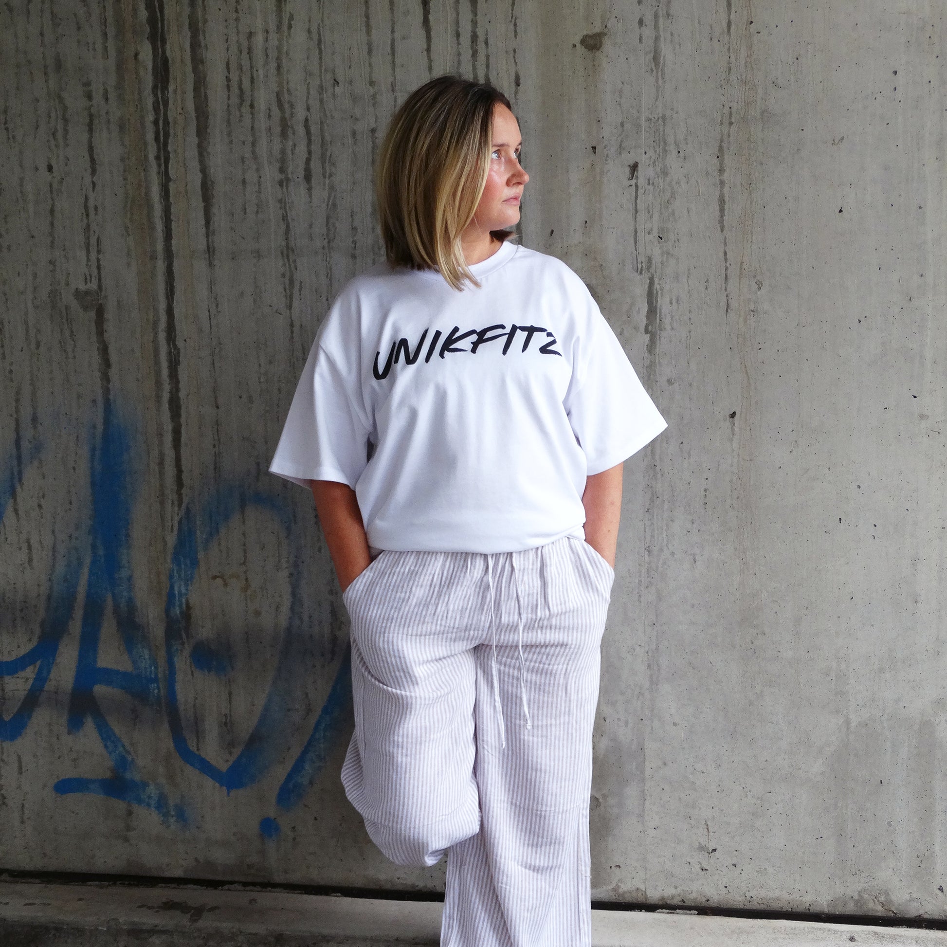 Model wearing the white 'Born to Disrupt' t-shirt by UNIKFITZ, featuring a sleek front logo. This oversized women’s t-shirt essential blends gym-ready durability with streetwear appeal, making it a must-have in any Australian streetwear women’s clothing collection.