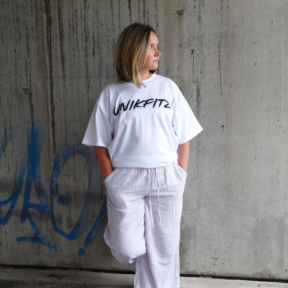 Model wearing the white 'Born to Disrupt' t-shirt by UNIKFITZ, featuring a sleek front logo. This oversized women’s t-shirt essential blends gym-ready durability with streetwear appeal, making it a must-have in any Australian streetwear women’s clothing collection.
