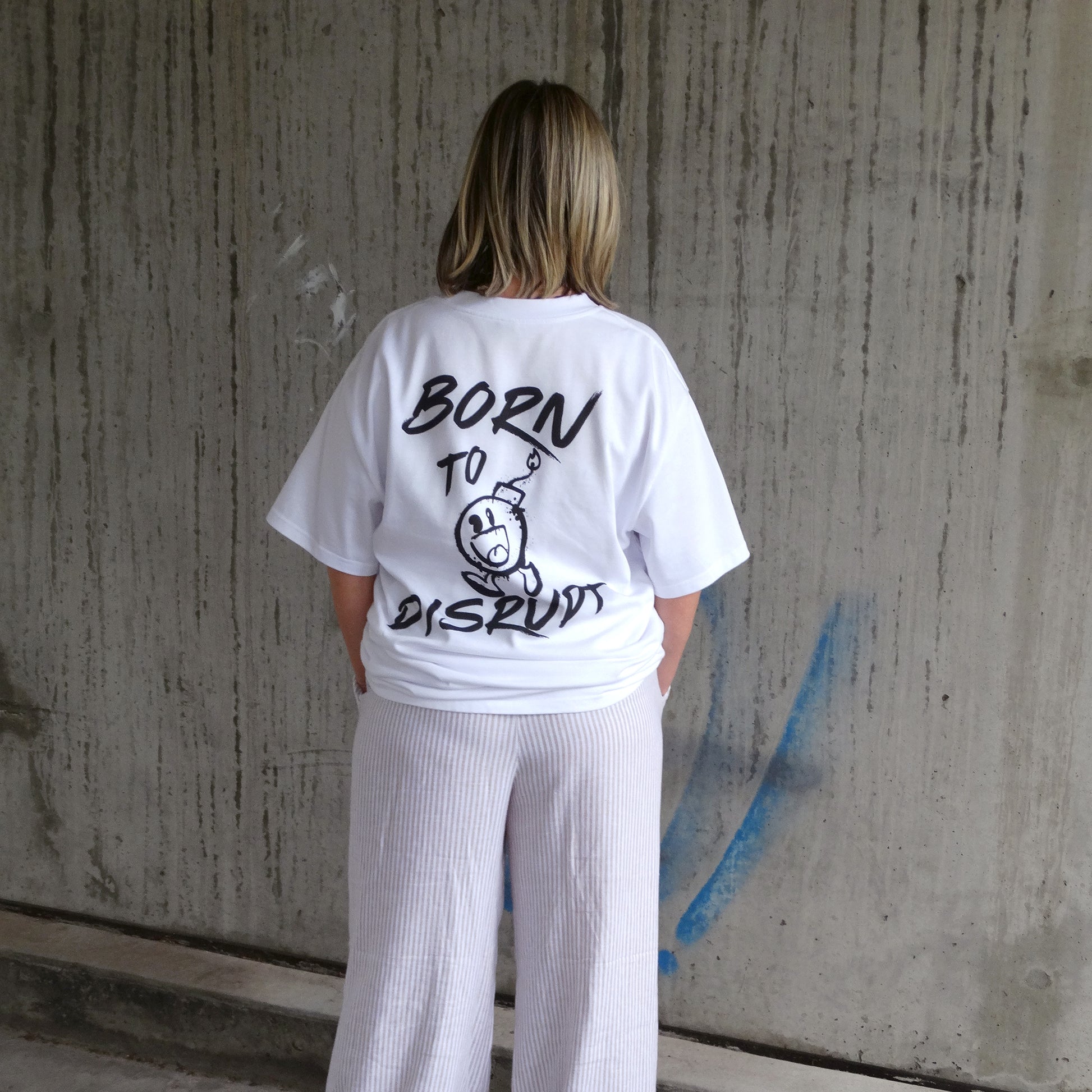 Back view of a model in the 'Born to Disrupt' oversized white t-shirt, showcasing rebellious typography and bold cartoon bomb artwork. Crafted for streetwear enthusiasts, gym lovers, and those who embrace disruption, this women's t-shirt essential is a statement piece in modern Australian streetwear.