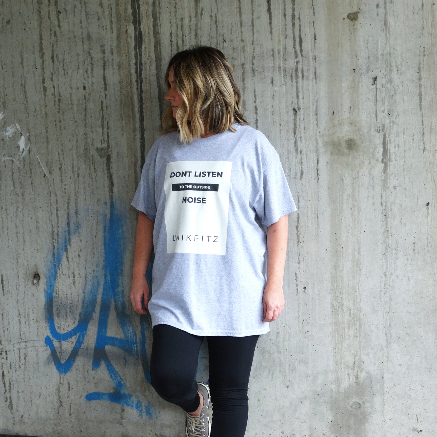 Model wearing the UNIKFITZ "Don't Listen to the Outside Noise" women's t-shirt in sport grey. A bold Australian streetwear essential designed for self-expression and gym wear. The premium cotton tee features a high-contrast front print and a relaxed fit for comfort