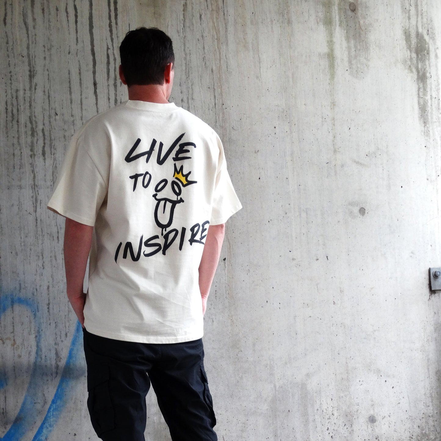 Back view of the 'Live to Inspire' men's t-shirt by UNIKFITZ, showcasing bold graffiti-style typography and a playful face graphic with a gold crown. This men's t-shirt essential combines Australian streetwear culture with a powerful message, making it a must-have for those seeking unique men's wear.